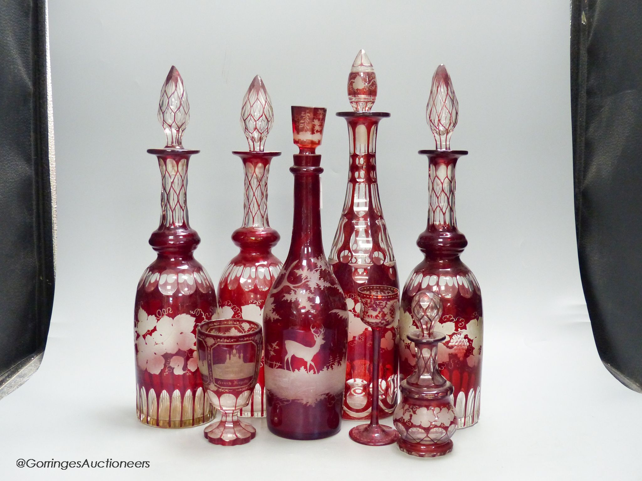 A collection of six Bohemian ruby flashed wheel engraved glass decanters, tallest 40cm, a similar spa beaker and liqueur glass